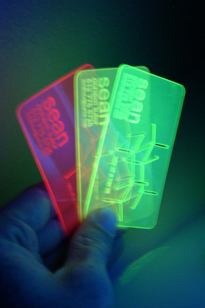 Business card in three colors of material, under UV light to show fluorescence.