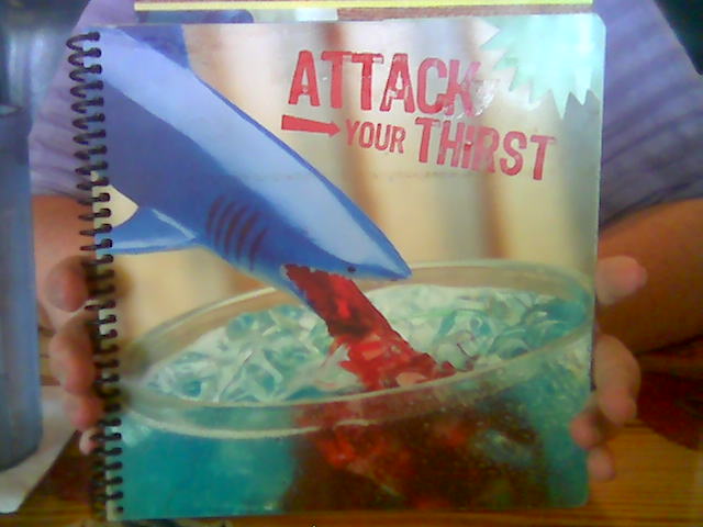Blue plastic shark vomits red liquid into blue liquid in a cocktail glass.