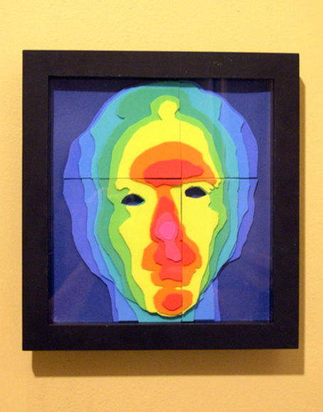 A dimensional face formed by raised topographic layers in colors proceeding through the spectrum from blue (deepest) to hot pink (highest), set in a square black frame.